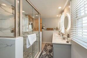 A modern bathroom with a glass-enclosed shower, a vanity with a mirror, and a rug on the floor.