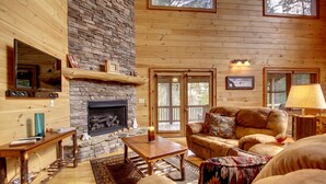 A cozy living room with a stone fireplace, wooden walls, and a comfortable seating area. - CHEROKEE DREAM - SECLUDED MTN VIEW, POOL TABLE, AIR HOCKEY, FIRE PIT, SCREENED PORCH (Epworth)