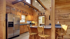 A wooden cabin-style kitchen with a stainless steel refrigerator, wooden cabinets, and a bar area with chairs. - CHEROKEE DREAM - SECLUDED MTN VIEW, POOL TABLE, AIR HOCKEY, FIRE PIT, SCREENED PORCH (Epworth)