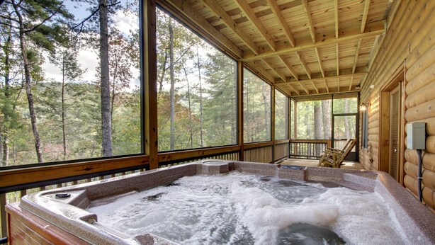 A hot tub in a log cabin with large windows overlooking a forest. - CHEROKEE DREAM - SECLUDED MTN VIEW, POOL TABLE, AIR HOCKEY, FIRE PIT, SCREENED PORCH (Epworth)
