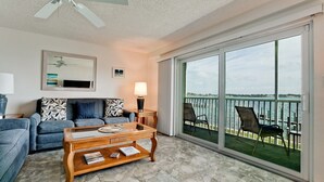 A living room with a sofa, coffee table, and a view of the water through large sliding glass doors.