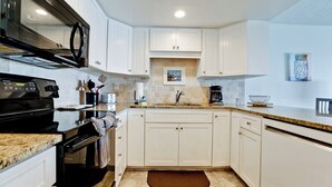 A modern kitchen with white cabinets, a black stove, a coffee maker, and a microwave.