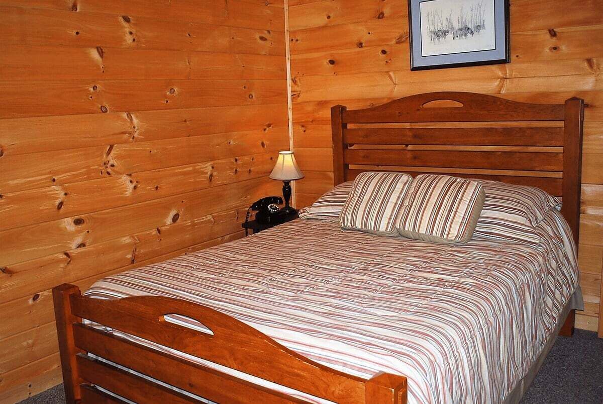 A wooden-paneled room with a bed, a nightstand, and a lamp.