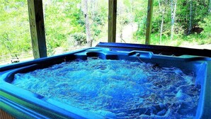 A hot tub with a view of a forested area through wooden windows.
