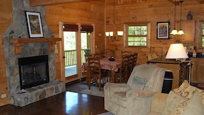 A cozy cabin interior with a stone fireplace, wooden dining table, and comfortable seating.