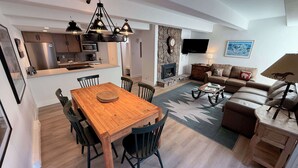 Un salon moderne avec une table à manger en bois, des chaises noires, un canapé marron et une cheminée.