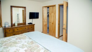 Ein Schlafzimmer mit Bett, Schminktisch, Spiegel, Fernseher und offenem Kleiderschrank.