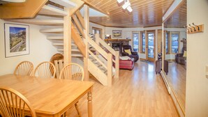 Ein großzügiger Wohnbereich mit einer Holztreppe, einem Kamin und einem Esstisch mit Stühlen.