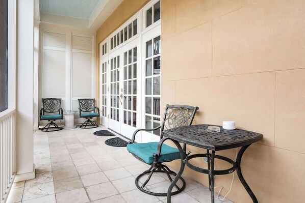 A patio with a table and two chairs, a window with shutters, and a tiled floor. - The Wedding Cake Main House (Savannah)