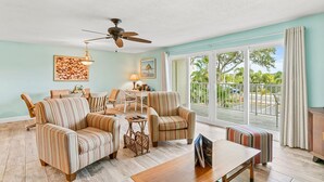A spacious living room with striped armchairs, a wooden coffee table, and a ceiling fan.
