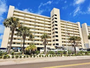 A multi-story hotel with a flat facade, balconies, and a parking area with cars.