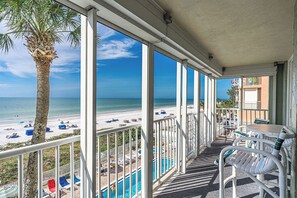 Un espace extérieur abrité, avec vue sur la plage et l’océan, comprenant une piscine, des chaises longues et un palmier.