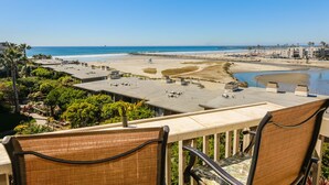 Vista a la playa desde un balcón con sillas, una piscina y vistas al océano y la playa.
