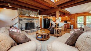 A spacious living area with a stone fireplace, wooden beams, and a kitchen in the background. - Tranquil Dog Friendly Escape w/ Dock Slip (Oakland)
