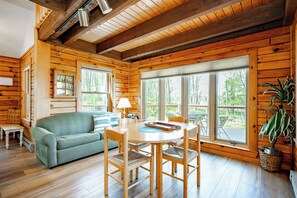Ein Holzblockhaus-Interieur mit Esstisch, Stühlen, einer Couch und großen Fenstern.