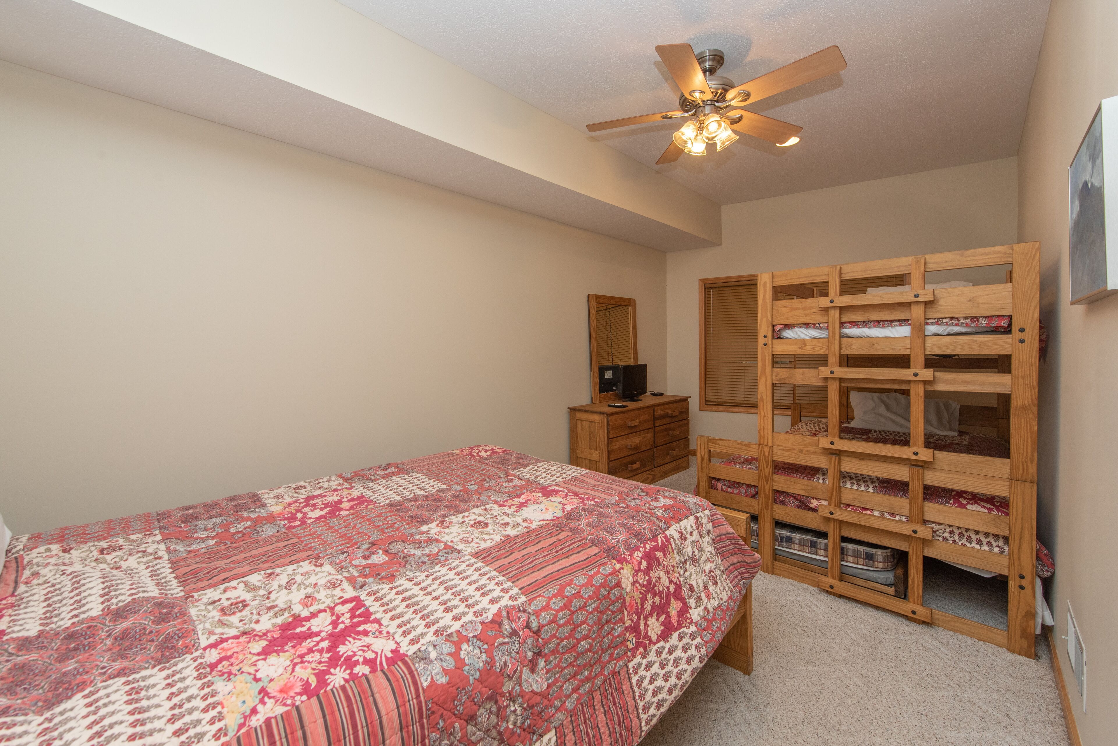 A bedroom with a bed, a ceiling fan, a wooden wardrobe, and a dresser.