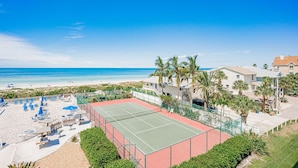 A beachfront property with a tennis court, beach chairs, and palm trees. - Gulf Front BEACH getaway - Reef Club 308 (Indian Rocks Beach)