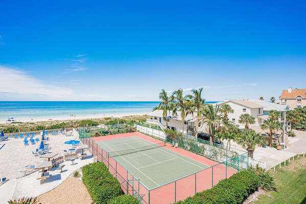 Une propriété située en bord de mer, dotée d’un court de tennis, de chaises de plage et de palmiers.