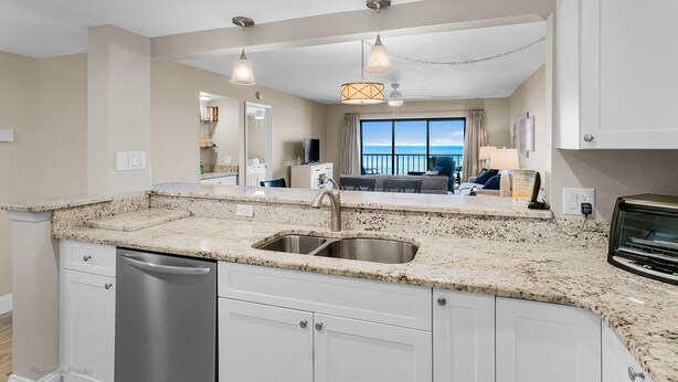 A modern kitchen with granite countertops, stainless steel appliances, and a large window offering a view of the ocean. - Gulf Front BEACH getaway - Reef Club 308 (Indian Rocks Beach)
