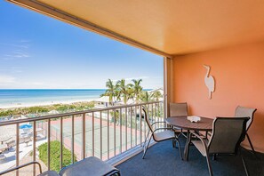 Een balkon met uitzicht op het strand, een tafel met stoelen en een decoratief wandobject.