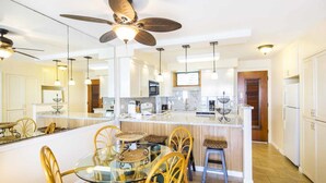 Una cocina moderna con una isla central, armarios blancos y un ventilador de techo.