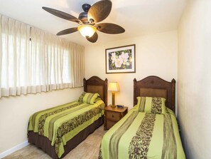 A bedroom with two beds, a ceiling fan, a nightstand with a lamp, and a framed picture on the wall.