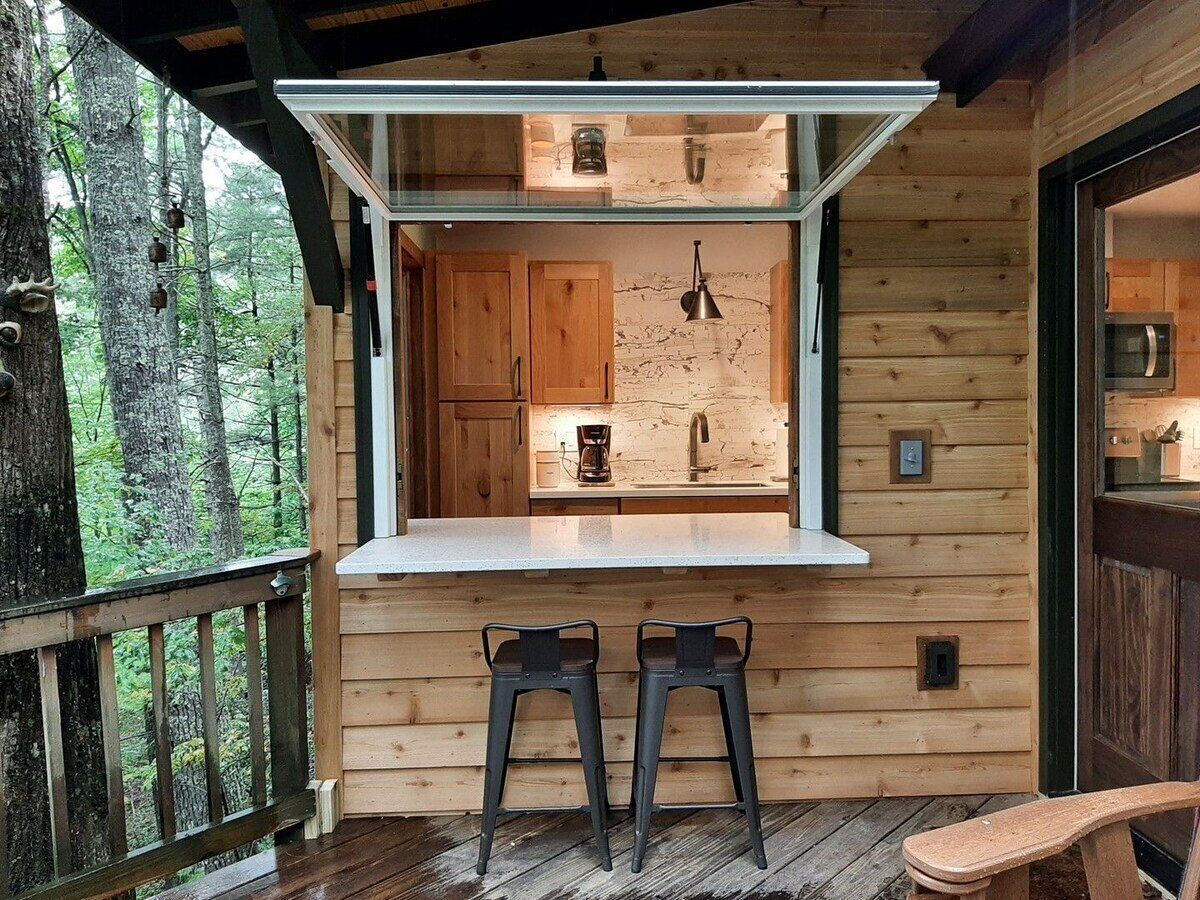 Une cabane en bois avec un coin cuisine, deux tabourets de bar et une terrasse.