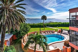 A swimming pool with a view of the water, surrounded by palm trees and a deck with lounge chairs. - Coquina Moorings 201 - Anna Maria Island - Condo 2 Bedroom/ 2 Bath with Den/3rd room , maximum occupancy of 6 people. (Bradenton Beach)