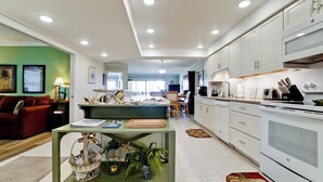 A modern kitchen with white cabinets, a dining area with a green table, and a living room with a red sofa.