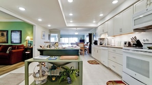 A modern kitchen with white cabinets, a dining area with a green table, and a living room with a red sofa. - Coquina Moorings 201 - Anna Maria Island - Condo 2 Bedroom/ 2 Bath with Den/3rd room , maximum occupancy of 6 people. (Bradenton Beach)