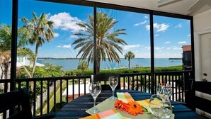 A balcony with a table set for two, overlooking a beach with palm trees and the ocean.