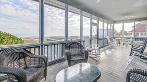 A covered deck with wicker furniture, large windows, and a view of the beach. - Timeless Oceanfront Beach Retreat in DeBordieu (Georgetown)