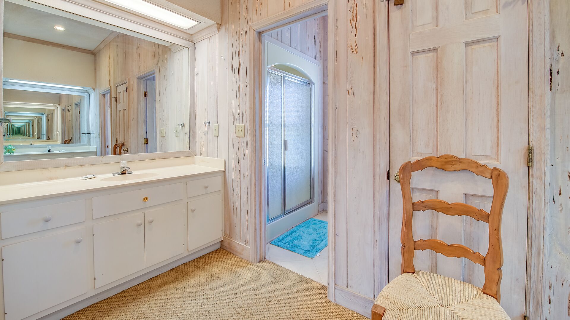 Un baño con tocador blanco, un espejo grande y una ducha con puertas de vidrio esmerilado.
