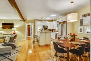 Una cocina moderna con armarios blancos, una isla central y un comedor con mesa y sillas de madera.