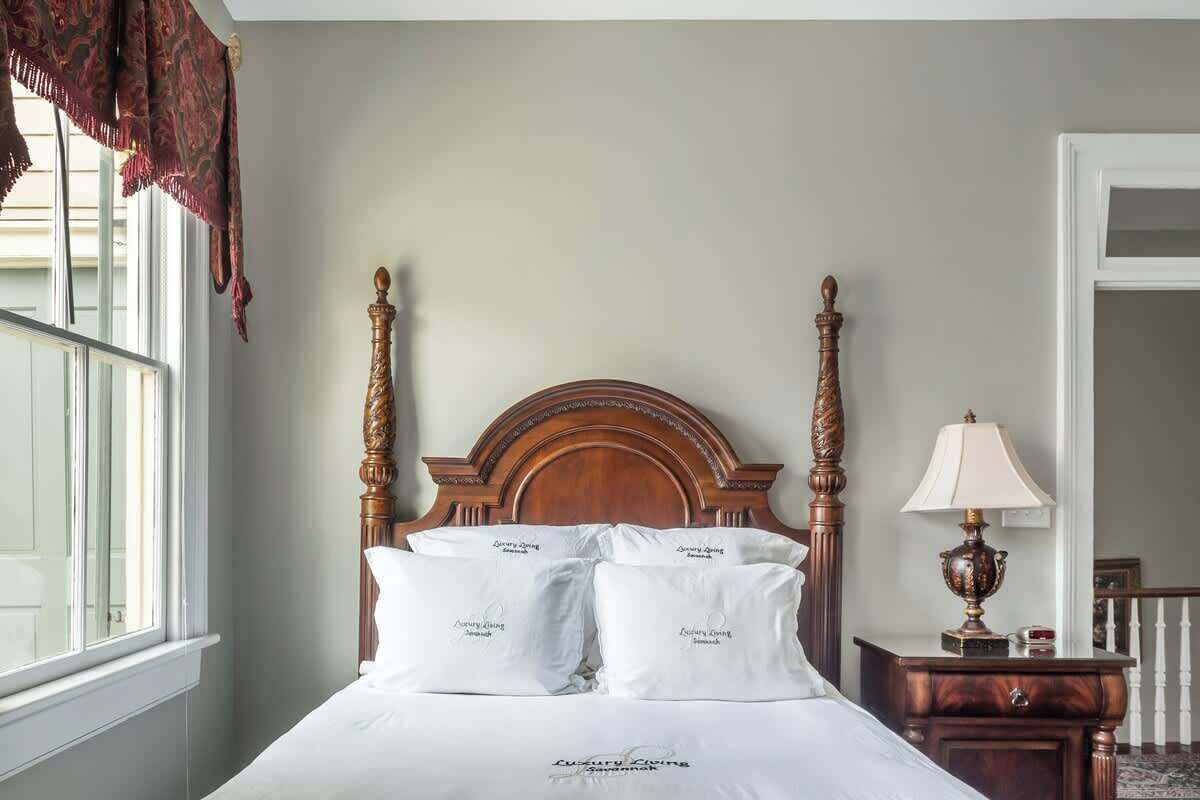 A bed with a wooden headboard, white linens, and a lamp on a bedside table.