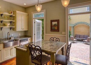 A kitchen with a marble countertop, a dining table with chairs, and a view of an outdoor patio. - The Washington Square Mansion (Savannah)