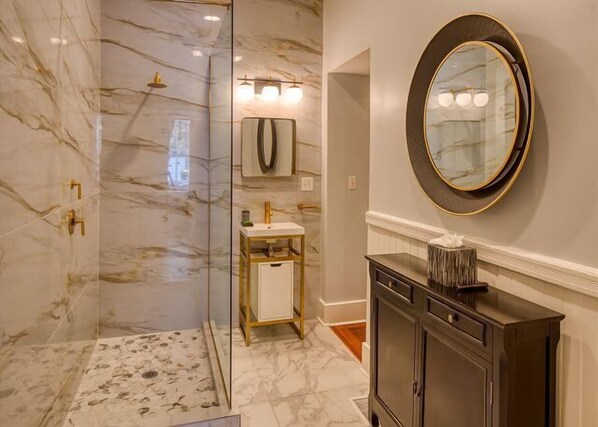 Un baño con ducha de mármol, lavabo con tocador dorado y un espejo grande en la pared.