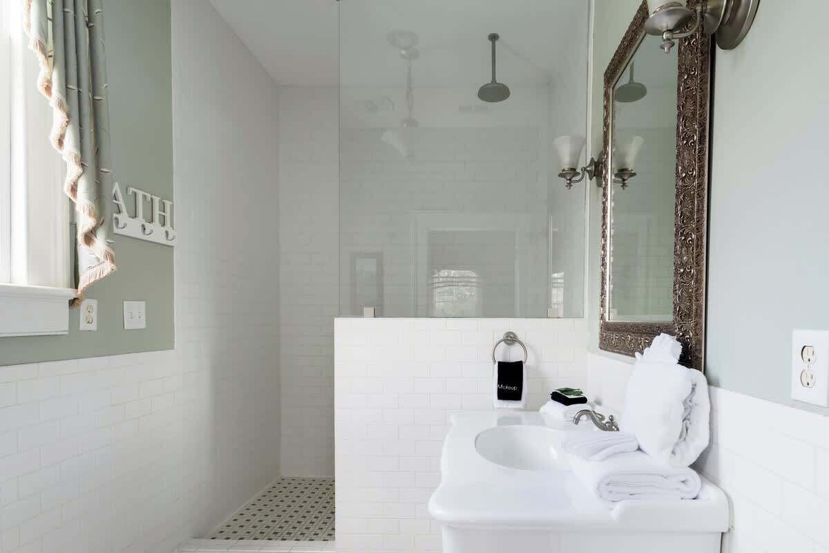 Une salle de bain avec un lavabo blanc, un miroir doté d’un cadre orné et un espace douche.