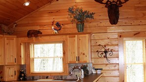 A wooden cabin kitchen with a central island, bar stools, and decorative elements like a moose head and a rooster. - Mountain Cabin,Pool Table,Views,Hot Tub,Fireplace, WiFi, Pet Friendly (Ferguson)