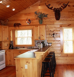 Cozy cabin-style kitchen with a central island, stove, and window with blinds.