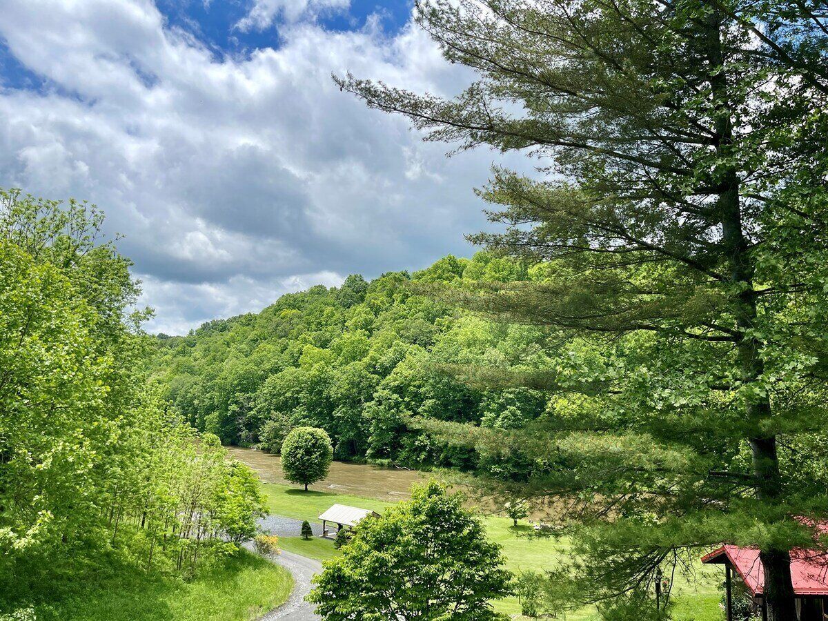 A lush green landscape with a river, a small building, and a red-roofed structure.