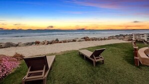 Een terras aan het strand met uitzicht op de oceaan, met ligbedden en een gazon.