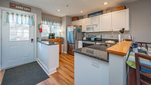 Una cocina compacta con armarios blancos, un refrigerador de acero inoxidable, un microondas y un lavabo.