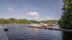 Un lago tranquilo con un muelle y barcos, rodeado de árboles y colinas.