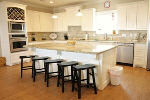 A kitchen with white cabinets, a granite countertop, a built-in oven, a microwave, a dishwasher, and a large island with bar stools. - Happily Ever After: 3  BR, 2  BA House in Crystal Beach, Sleeps 12 (Bolivar Peninsula)