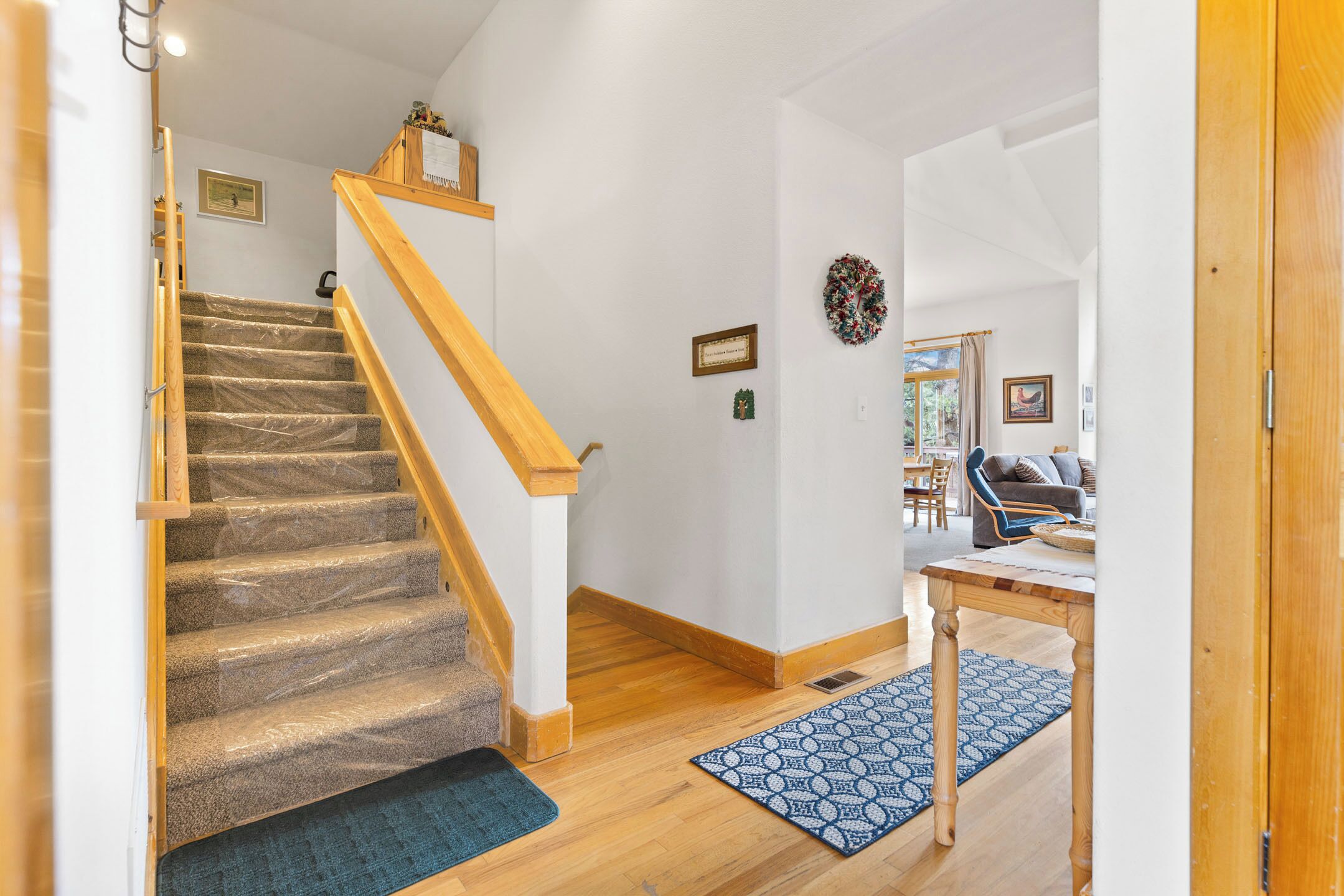 A staircase with carpeted steps leading to a landing, a wooden table, and a blue patterned rug on a wooden floor.
