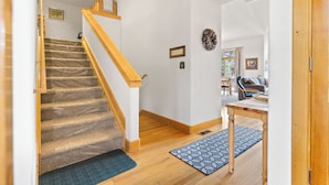Eine Treppe mit Teppichstufen führt zu einer Zwischenebene, einem Holztisch und einem blauen, gemusterten Teppich auf Holzdielen.