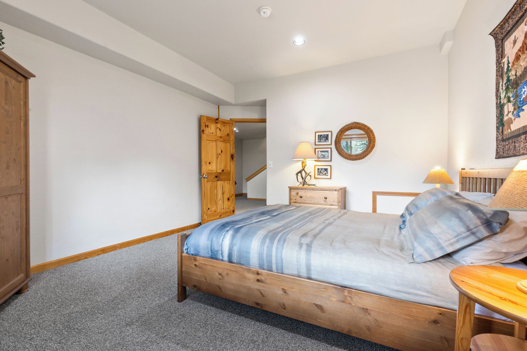 Een slaapkamer met een houten bed, een nachtkastje, een dressoir en een deur naar een andere kamer.