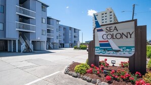 Une enseigne pour Sea Colony, avec un motif de bateau, entourée d’un parterre de fleurs.