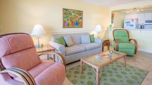 Un salon avec un canapé, des fauteuils, une table basse et un tableau accroché au mur.